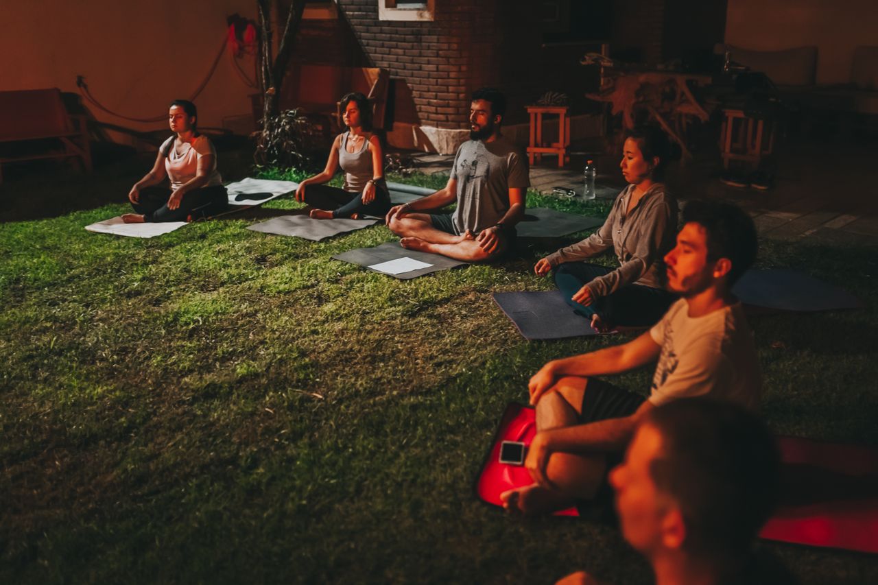 A diverse group meditating outdoors on yoga mats during evening time.