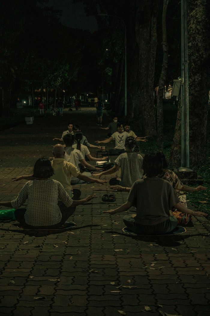 Group of people meditating outdoors at night on a paved path in an urban park setting.