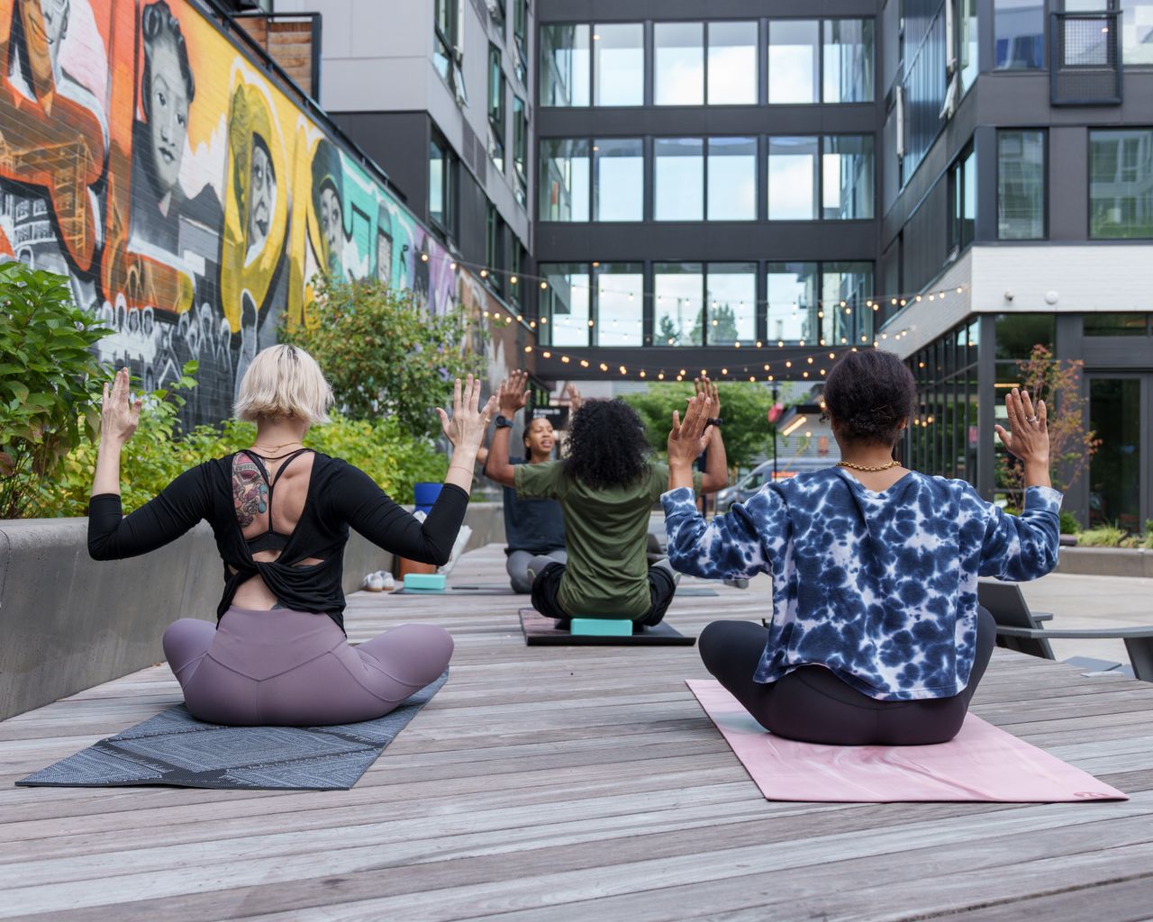 About A diverse group of adults practicing yoga outdoors in a vibrant urban setting.